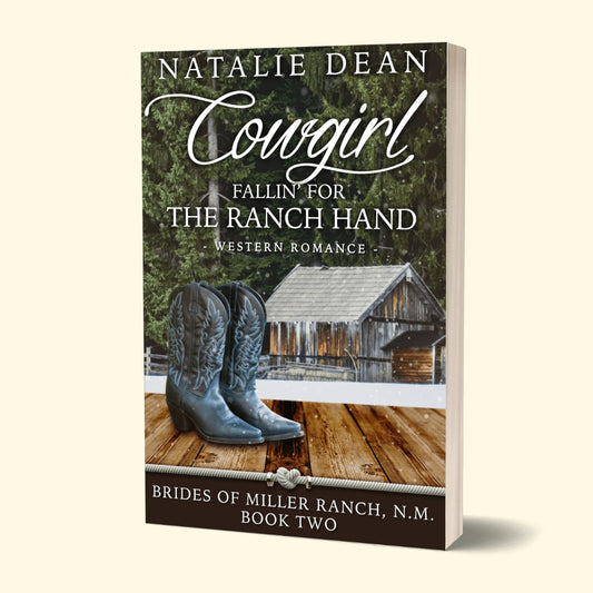 Paperback book mockup of Cowgirl Fallin' for the Ranch Hand, Brides of Miller Ranch, N.M. Book Two by Natalie Dean, a western romance; pair of cowgirl boots with ice-covered barn and trees in background