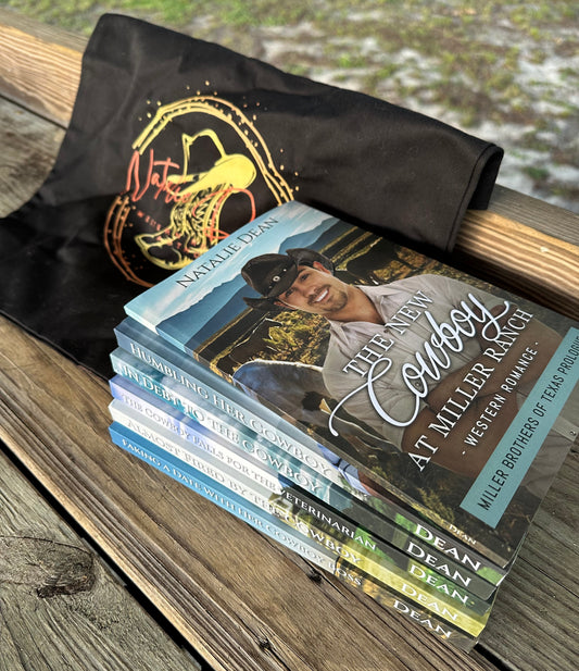 Stack of all six Miller Brothers of Texas books on a wooden surface with a black tote bag featuring the Natalie Dean logo. The logo on the bag has a line image of a pair of cowboy boots with a cowboy hat sitting on top, along with Natalie Dean written in a pretty script. 