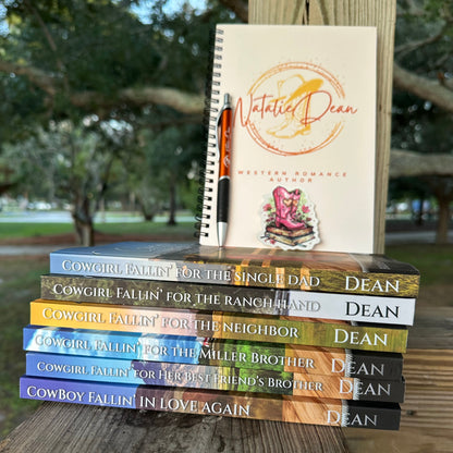 All six Brides of Miller Ranch paperback books, stacked viewed from the side of the spines. Also has a spiral bound notebook with the Natalie Dean logo of her signature plus a pair of cowboy boots and cowboy hat. A burnt orange ball point pen with the Natalie Dean logo on it. A cowgirl boots sticker, with the boots sitting on a stack of books. 
