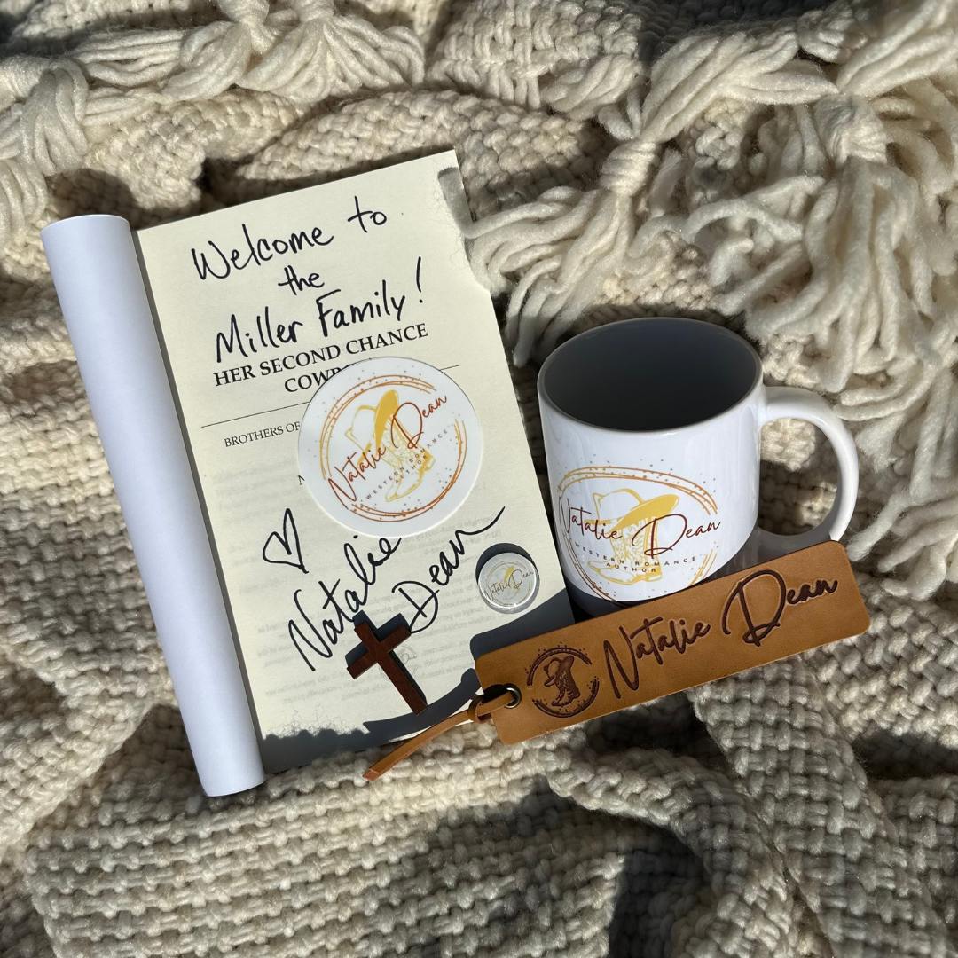 Natalie Dean special edition swag bundle with signed paperback book, coffee mug, faux leather bookmark, wooden cross, sticker, and glass dome magnet displayed on a cozy cream knit blanket.