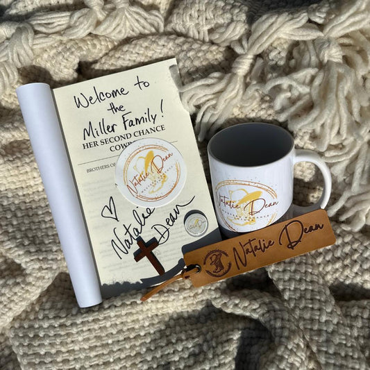 Natalie Dean special edition swag bundle with signed paperback book, coffee mug, faux leather bookmark, wooden cross, sticker, and glass dome magnet displayed on a cozy cream knit blanket.